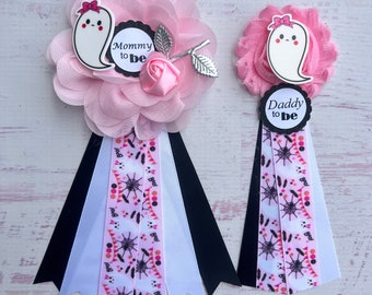 May include: Two pink and white Halloween themed baby shower sashes with a ghost and the text "Mommy to be" and "Daddy to be".