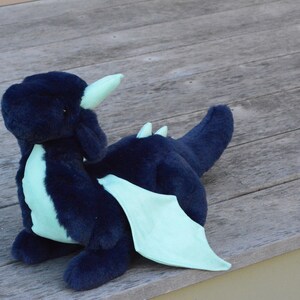May include: A plush blue dragon with light green wings and horns. The dragon is sitting on a wooden surface.