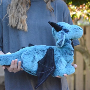 May include: A teal blue plush dragon with black wings and a black horn. The dragon is soft and cuddly and would make a great gift for a child.