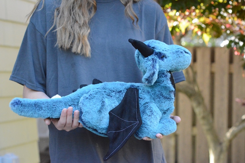 May include: A teal blue plush dragon with black wings and a black horn. The dragon is soft and cuddly and would make a great gift for a child.