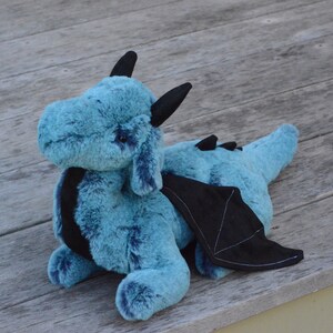 May include: A plush blue dragon with black wings and horns. The dragon is lying on a wooden surface.