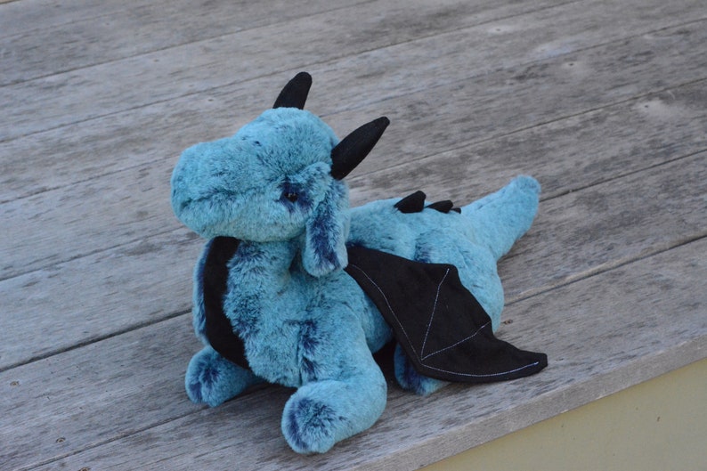 May include: A plush blue dragon with black wings and horns. The dragon is lying on a wooden surface.