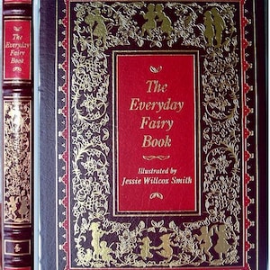 May include: A vintage hardcover book titled "The Everyday Fairy Book" with a red and gold cover. The cover features gold illustrations of fairies and floral designs on a dark burgundy background. The spine also displays the title.
