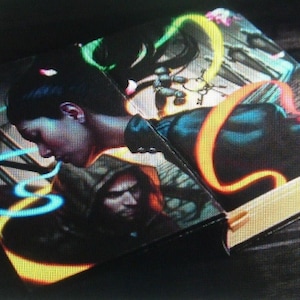 May include: A book with a black cover and a colorful illustration of a woman with long black hair and a man with a hood. The illustration features neon green, blue, and orange swirls.