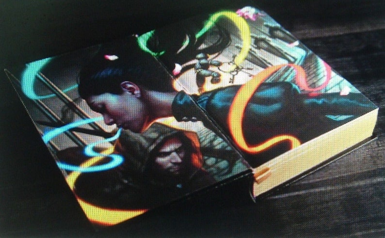 May include: A book with a black cover and a colorful illustration of a woman with long black hair and a man with a hood. The illustration features neon green, blue, and orange swirls.