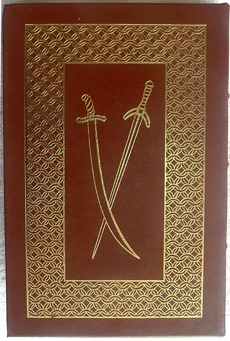 May include: A brown leather-bound book with a gold-colored design on the cover. The design features two crossed swords.