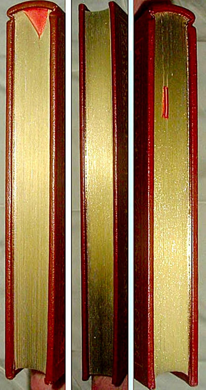 May include: A close-up of a book with a red leather cover and gold-gilded edges. The pages are gold, and a red ribbon bookmark is visible. The book's spine is also red.
