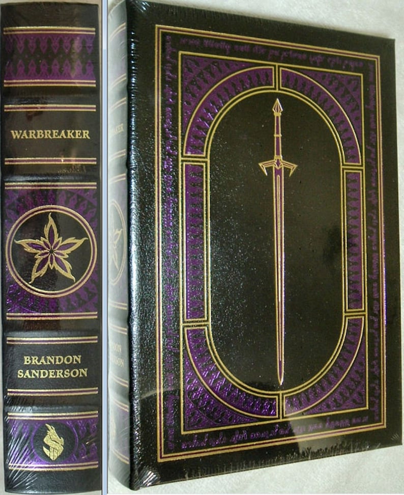 May include: A black leather-bound book with gold accents and a purple design. The title "Warbreaker" is printed on the spine. The book is by Brandon Sanderson.