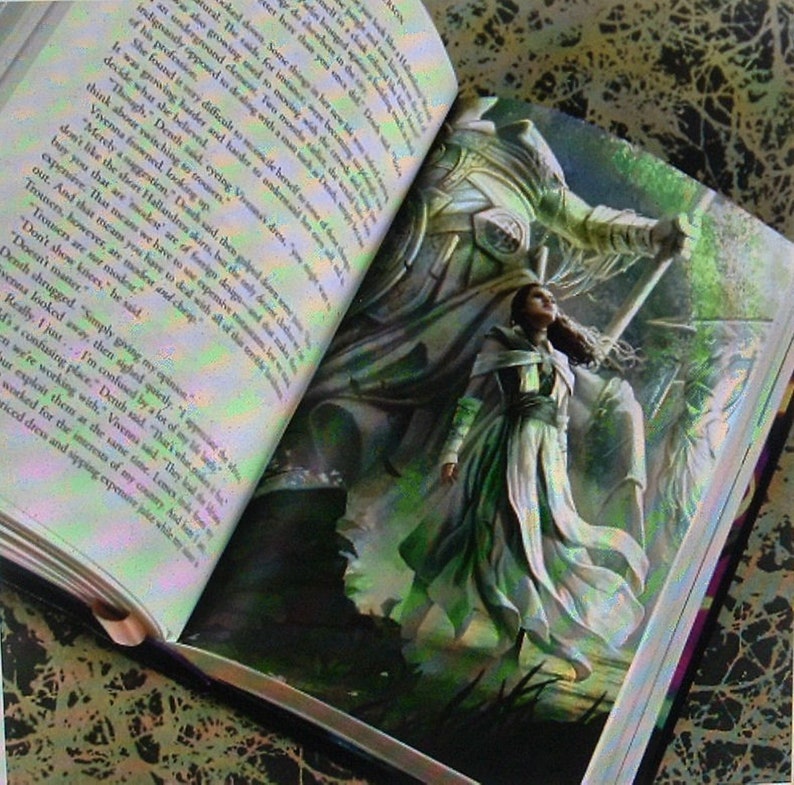 May include: An open book with a white and green illustration of a woman standing in front of a large, armored figure. The book is open to a page with text about trousers and skirts.