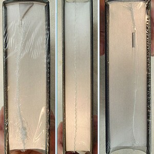 May include: Close-up of the spine of a hardcover book with a white cover and black binding. The book is wrapped in clear plastic.