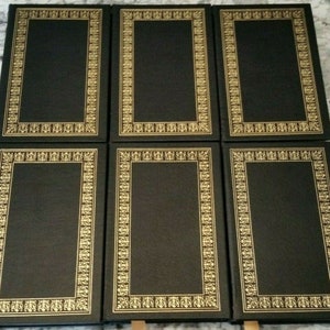 May include: Six hardcover books with black covers and gold decorative borders. The rectangular borders feature intricate floral and geometric patterns. The books are arranged in two rows of three.