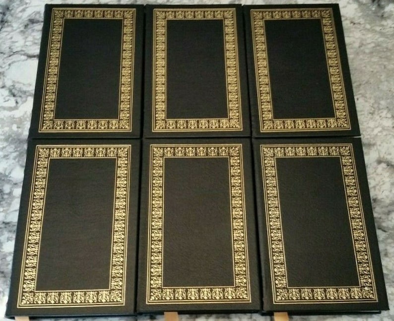 May include: Six hardcover books with black covers and gold decorative borders. The rectangular borders feature intricate floral and geometric patterns. The books are arranged in two rows of three.