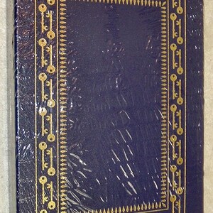 K&ouml;nnte beinhalten: Ein dunkelblaues Buch mit einem goldenen Schl&uuml;sseldesign an den R&auml;ndern. Die H&uuml;lle ist in klarem Kunststoff verpackt. Das Schl&uuml;sseldesign ist ein sich wiederholendes Muster. Das Buch ist rechteckig und scheint neu zu sein.