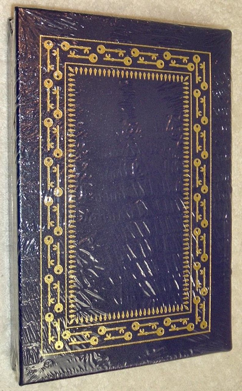 K&ouml;nnte beinhalten: Ein dunkelblaues Buch mit einem goldenen Schl&uuml;sseldesign an den R&auml;ndern. Die H&uuml;lle ist in klarem Kunststoff verpackt. Das Schl&uuml;sseldesign ist ein sich wiederholendes Muster. Das Buch ist rechteckig und scheint neu zu sein.