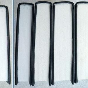 May include: Close-up of six book spines with black covers and white pages. The spines are lined up side-by-side. The first four spines are plain white, while the last two spines have a colourful patterned design.