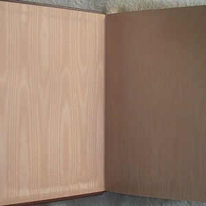 May include: An open book with a brown leather cover and a beige endpaper. The book is closed and the pages are blank.