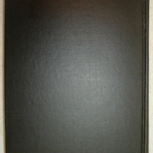 May include: A close-up of a book cover. The cover is a solid, dark charcoal color with a textured, slightly rough surface. The spine is visible on the right side, also dark, with a slightly different texture. The edges of the cover are slightly worn.