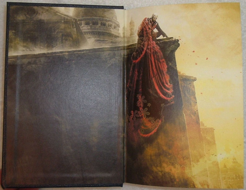 May include: A book cover with a dark brown background. The cover features a man in a black suit and a woman in a red dress standing on a ledge. The woman's dress has a floral pattern. The background is a cityscape with a building in the distance.