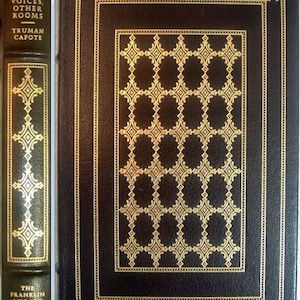 May include: A black leather-bound book with gold accents and a gold patterned design on the cover. The title "Other Voices, Other Rooms" by Truman Capote is printed on the spine. The book is part of "The Franklin Library" collection.