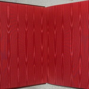 May include: Open book with red wood grain patterned pages. The pages are a vibrant red color with a detailed wood grain design. The book's spine is a darker shade of red.
