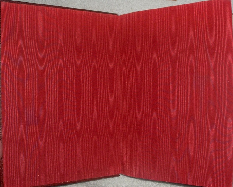 May include: Open book with red wood grain patterned pages. The pages are a vibrant red color with a detailed wood grain design. The book's spine is a darker shade of red.