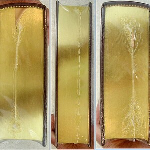 May include: Close-up of the spine of a hardcover book with a gold cover and a clear plastic dust jacket. The book is bound with a sewn binding and the spine is visible through the plastic.