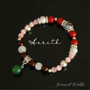 Puede incluir: Un brazalete de cuentas rojas, rosas y blancas con un dije de plata y un colgante de jade verde. El brazalete tiene la palabra "Aerith" escrita en él.