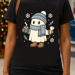 May include: Black t-shirt featuring a cartoon character dressed for winter. The character wears a blue hat, scarf, and boots, holding a mug of hot beverage and a medical device. Snowflakes and sprigs are also in the design.