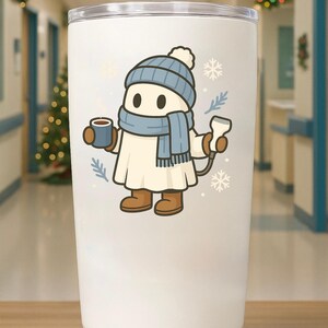 May include: A white insulated tumbler featuring a cartoon character in a winter outfit. The character wears a blue hat, scarf, and holds a mug and a thermometer. Decorative snowflakes and sprigs are scattered around the character.