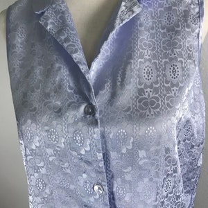 May include: A light blue sleeveless button-up shirt with a floral pattern. The shirt has a collar and a button closure.