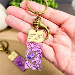 May include: A purple and white anatomical specimen keychain with a label that reads "Specimen No. Control 62 Kidney Locality 1918".