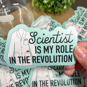 May include: A teal blue sticker with a white lab coat and the text "Scientist is my role in the revolution".