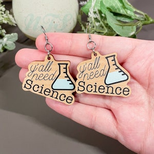 May include: A pair of wooden earrings with a light blue beaker and the text "y'all need science" on each earring.