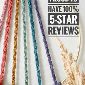 May include: A close-up of a macrame wall hanging with a gold metal ring and colorful braided cords in shades of pink, orange, green, teal, and purple. The text "PROUD TO HAVE 100% 5-STAR REVIEWS" is displayed in a black rectangle.