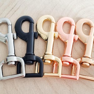 May include: Four metal swivel clasps in silver, black, gold, rose gold, and copper colours. The clasps are arranged in a row, showcasing their different finishes. The clasps are designed for various crafting and accessory projects.
