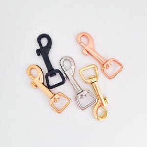 May include: Five metal swivel lobster claw clasps in various finishes including matte black, polished silver, bright gold, rose gold, and light gold. Each clasp features a spring-loaded gate and a square-shaped swivel base for attachment.