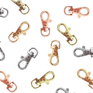 Puede incluir: Una variedad de cierres de mosquet&oacute;n giratorios en varios acabados met&aacute;licos, incluyendo oro, plata y oro rosa. Los cierres est&aacute;n dispuestos sobre un fondo blanco, mostrando sus diferentes colores y dise&ntilde;os. Estos cierres se utilizan com&uacute;nmente en la fabricaci&oacute;n de joyas y manualidades.