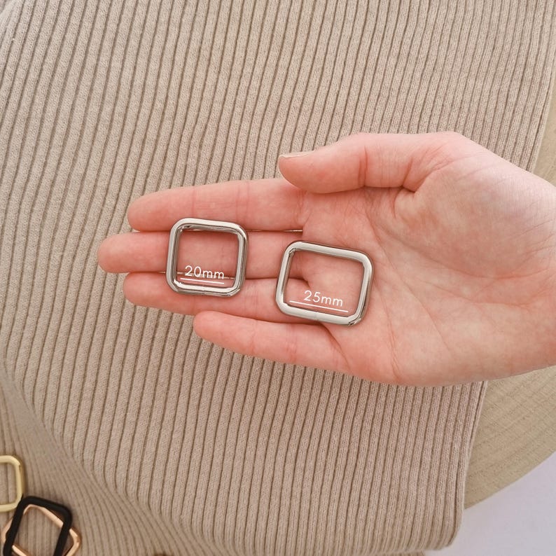 Peut inclure: Deux anneaux carr&eacute;s en m&eacute;tal argent&eacute; aux coins arrondis sont pr&eacute;sent&eacute;s. L'un est &eacute;tiquet&eacute; "20mm" et l'autre "25mm". Les anneaux sont tenus dans une main, sur un fond neutre.