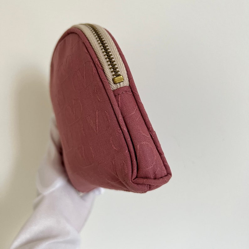 Peut inclure: Une pochette zipp&eacute;e de couleur rose poussi&eacute;reux avec une fermeture &eacute;clair blanche et un motif gaufr&eacute; subtil. La pochette est faite d'un tissu doux et textur&eacute;.