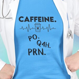 May include: A blue t-shirt with a white lab coat over it. The t-shirt has a graphic of a coffee cup with a heartbeat line and the text "CAFFEINE. PO. Q4H. PRN."