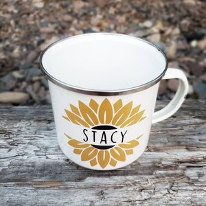 Op de afbeelding: Een witte emaille mok met een gouden zonnebloemontwerp en de naam "Stacy" in zwart op een witte banner.