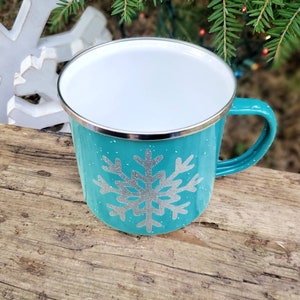 May include: A turquoise blue enamel mug with a silver snowflake design. The mug has a white interior and a silver rim.