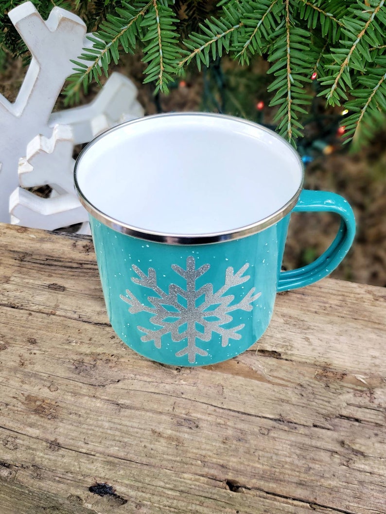 May include: A turquoise blue enamel mug with a silver snowflake design. The mug has a white interior and a silver rim.
