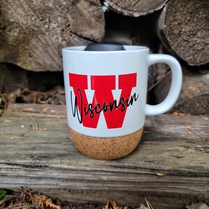 May include: White ceramic mug with a red "W" and the word "Wisconsin" in black script. The mug has a cork bottom.
