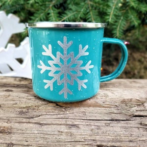 May include: Teal enamel mug with a silver snowflake design. The mug has a white rim and handle.