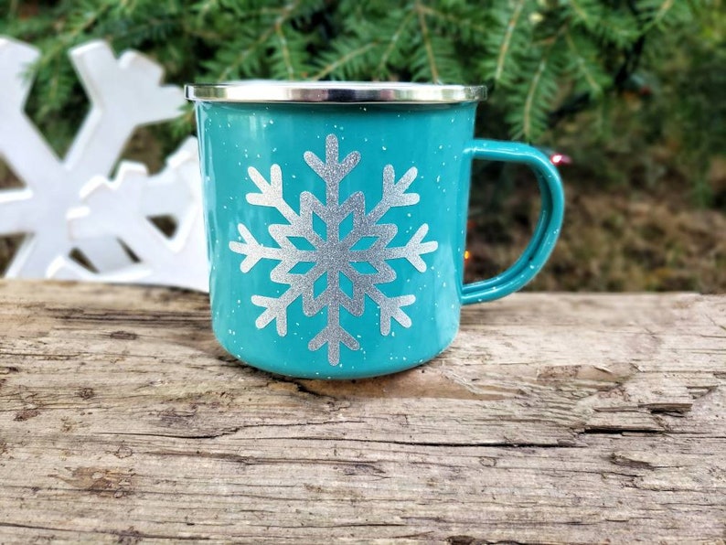 May include: Teal enamel mug with a silver snowflake design. The mug has a white rim and handle.