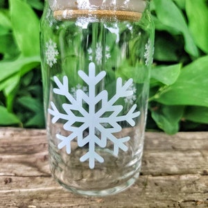 May include: A clear glass drinking bottle with a bamboo lid and a white snowflake design. The bottle has a straw sticking out of the lid.