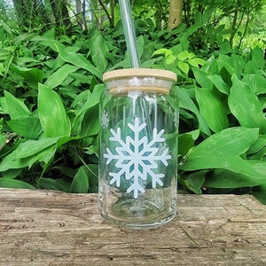 May include: A clear glass jar with a wooden lid and a white snowflake design. A straw is sticking out of the lid.