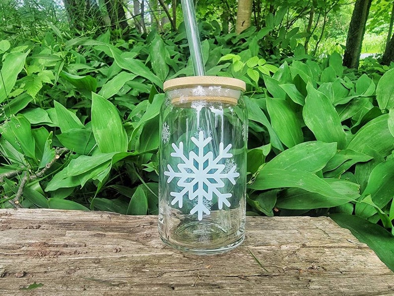 May include: A clear glass jar with a wooden lid and a white snowflake design. A straw is sticking out of the lid.