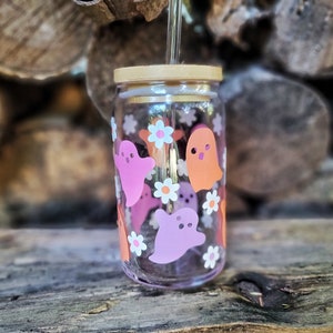 May include: A clear glass jar with a wooden lid and a straw. The jar is decorated with pink and orange ghost stickers and white flower stickers.